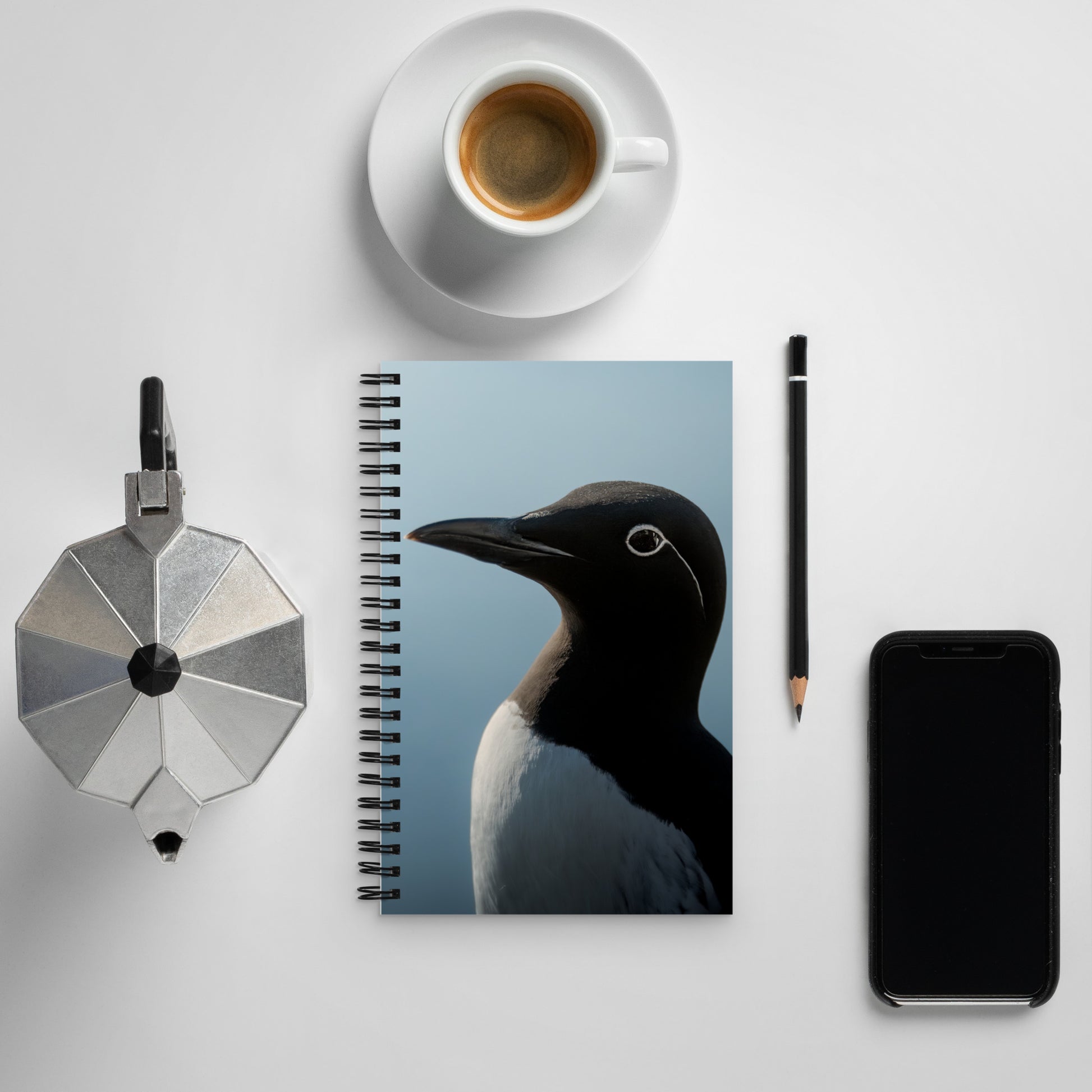 Common murre notebook laying next to a phone and mug of coffee.